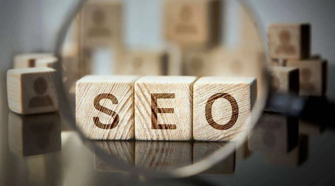 Cubes en bois formant le sigle SEO sous une loupe